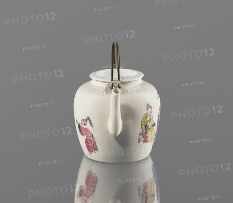 Teapot with a lid; creator, Chinese; Qing dynasty 1644–1911; colored porcelain teapot with tubular spout and flat, concave lid; porcelain body with white transparent glaze; decoration painted with onglaze enamel paints depicting images of women, servants, and figurative scenes; 19th century, China; height 8.8 cm, width 12.0 cm, depth 9.2 cm., A white ceramic teapot with a rounded body and a narrow spout sits centered on a reflective surface against a gray background, showing a metal double-loop handle attached at the top and colorful painted figures on its sides in tones of red, blue, yellow, green, and pink, with the reflection of the pot and its painted details visible below.