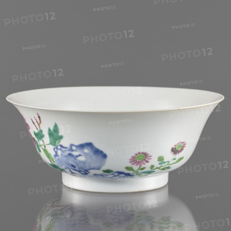 Bowl. Semicircular body widening toward the upper edge. Porcelain body with white, transparent, sintered glaze; decoration painted with overglaze enamel paints depicting peonies and floral decorations in colored porcelain. Chinese, Qing dynasty, Yongzheng period 1723–1735. Height 7.6 cm; diameter 19.5 cm., A white porcelain bowl with a flared rim and a short foot sits against a gray background, decorated around its exterior with floral and foliage motifs in colors including green, blue, pink, and a touch of brown, and the bowl is reflected faintly on the glossy surface below.
