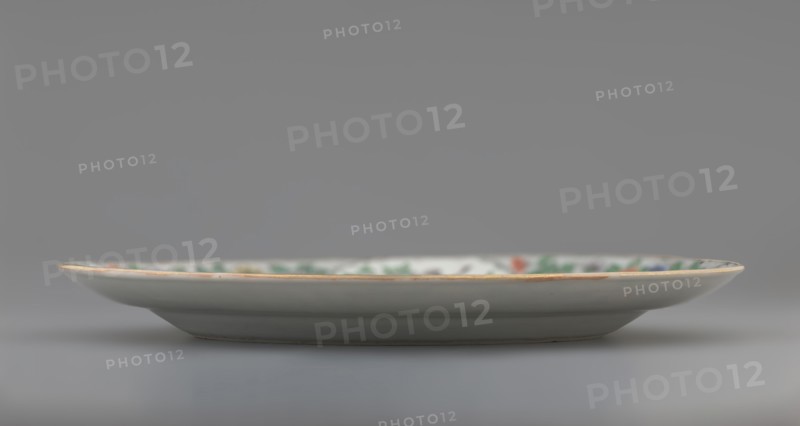 Plate. Porcelain fragment; white glaze. Decoration painted with overglaze enamel paints and iron red, featuring plant motifs and figural scenes. Chinese, Qing dynasty 1644–1911, 18th century. Colored porcelain. Vessel; height 2.4 cm, diameter 20.4 cm, weight 0.35 kg., A shallow ceramic plate photographed from the side, showing a narrow rim with a thin golden edge and a mostly white surface; the interior rim has a band of muted green and small areas of red and blue visible, while the underside and outer body appear light gray to off-white; the background is a smooth gradient of gray.