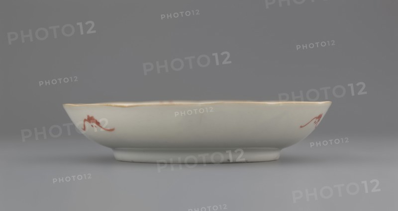 Plate. Chinese; Qing dynasty 1644–1911. Porcelain fragment with white glaze and decoration painted in overglaze enamel paints depicting cranes and waves. 19th century. Vessel; height 2.8 cm, diameter 13.5 cm, weight 0.15 kg., A shallow round ceramic dish with a scalloped rim sits on a flat surface; the dish is primarily white with a faint warm off-white tone and a thin golden trim along the rim, and it features a few small red decorative brushstroke motifs on its outer side; the background and surface are shades of gray.