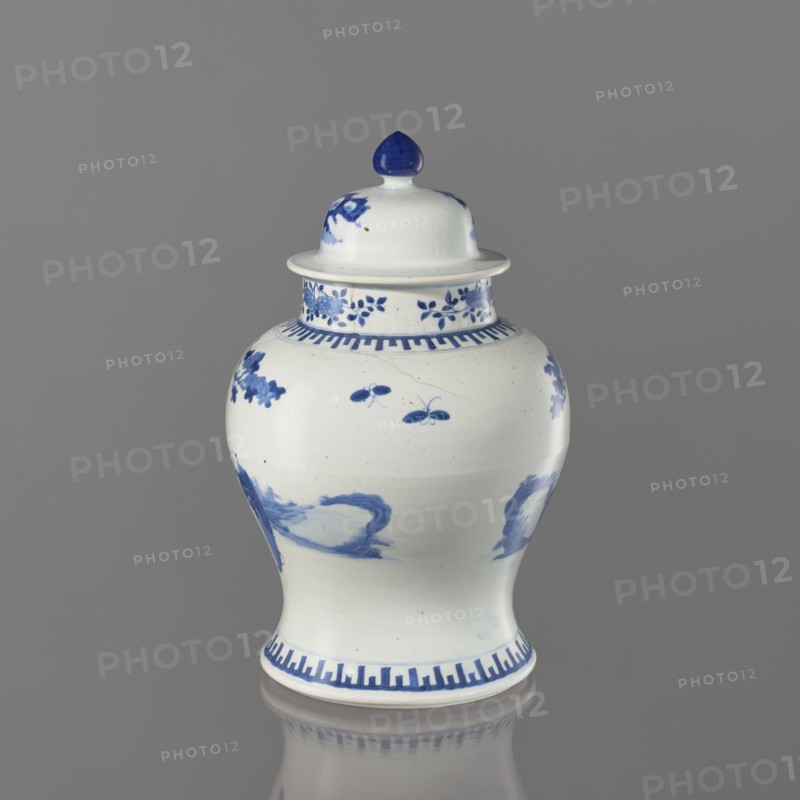 Vase with lid, Chinese, Chinese art, ceramics; motifs: boys, butterflies, female images, terraces architectural; thick porcelain body; greyish-blue glaze with underglaze cobalt painted decoration; 19th century, China; vessel, height 36.5 cm, A ceramic lidded jar with a glossy white surface and blue painted decoration sits against a neutral gray background; the jar has a bulbous body tapering to a narrower base and a domed lid topped with a blue finial, with floral and abstract blue motifs around the neck and shoulder, a band of geometric blue pattern near the base and rim, and reflections visible on the gray surface beneath the jar.