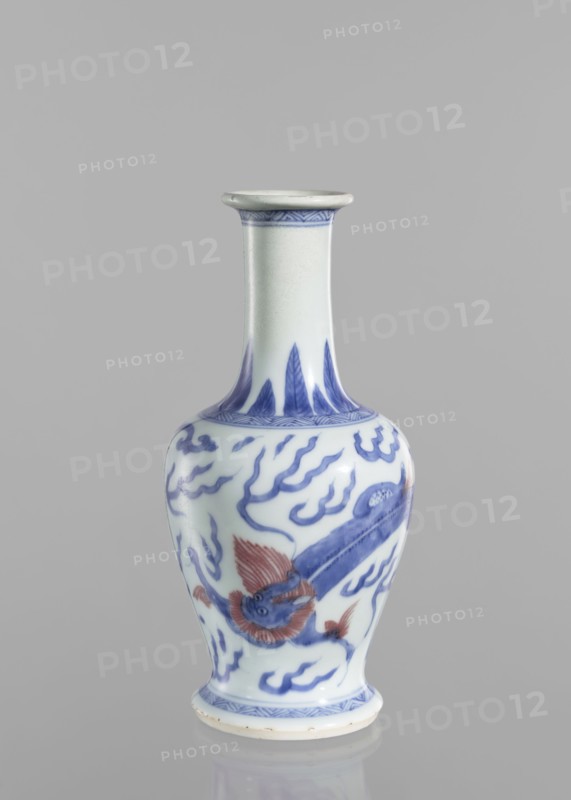 Vase, blue and white porcelain, Chinese, Qing 1644–1911, 19th century. Vessel decorated with dragons and pearls. Height 19.6 cm; diameter 9.3 cm., A ceramic vase with a narrow neck and flared rim standing on a rounded foot, decorated with hand-painted designs in blue and red on a white background; the neck shows a band of blue pattern near the rim and vertical blue leaf-like motifs at its base, the bulbous body features flowing blue cloud-like motifs and a stylized creature with red fins and blue body wrapping around the surface, and a patterned blue band encircles the foot.