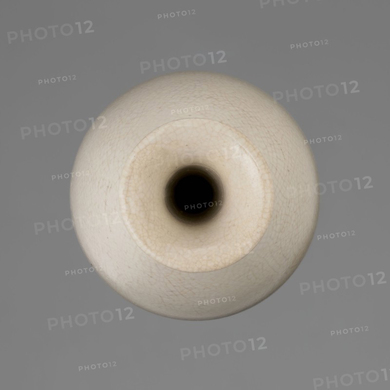 Vase on saucer. Vase made of stoneware or thick porcelain?, ovoid with a long cylindrical neck flaring at the spout; light cream white matte glaze covered with fine cracklework. 19th century, Japan, Edo 1603–1868. Ceramics; bottles/vessel. Height 24.1 cm; diameter 8.6 cm; weight 0.65 kg., A top-down view of a round ceramic vessel with a central circular opening, showing a smooth, slightly textured surface with fine crackle patterns; the vessel is primarily off-white to cream with subtle beige tones, and the interior of the opening appears dark, almost black; the background is a flat medium gray.