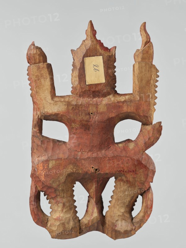 Demon with snakes - wall sculpture, unknown sculptor, snakes, Southeast Asia culture, Southeast Asian art, demons, religion, 19th century, Indonesia, sculpture, height 44.0 cm, width 27.0 cm, A carved wooden mask with a rough, faceted surface and a predominately reddish-brown patina, showing areas of lighter tan wood where the finish is worn or absent, featuring two eye openings and a crown-like top with pointed projections, a pair of raised vertical side elements with serrated edges, and a lower section with curved, scalloped forms and carved tooth-like ridges; the colors visible include reddish-brown, tan, and a few darker brown accents.