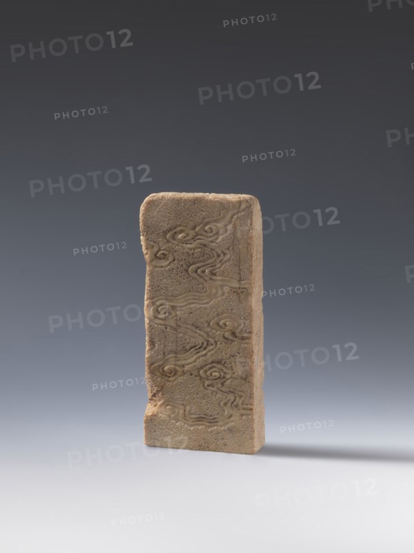Seal stamp; creator, bats iconography; lion iconography; arhat iconography; Chinese art; seal stamps; Chinese; Qing dynasty 1644–1911; bas-relief decoration; 19th century : China; height 20.0 cm; width 9.3 cm; depth 2.9 cm; inscription: Krieg doctor, A single upright rectangular stone plaque with a rough beige surface stands against a smooth gradient background that transitions from dark gray at the top to pale gray at the bottom; the plaque shows carved swirling cloud-like patterns in a slightly darker beige and tan, with surface pitting and a few worn edges, and it casts a soft shadow to the right on the pale gray ground.