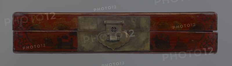 Box, Chinese, Qing 1644–1911, early 20th century. Lacquered container with staffage: boats, figural scenes of scholars and sages, landscape motifs, defensive walls architectural, swastikas. Materials/format: box; height 33.7 cm, width 19.5 cm, depth 6.7 cm., A rectangular box with a hinged lid viewed from the front, featuring a central metal clasp with a patinated surface and a decorative cloud-shaped plate; the box surface is predominantly red with areas of darker red and brown, showing painted dark brown and black ornamental patterns and stylized landscape or cloud motifs in muted gold and brown tones, and the background is a flat gray.