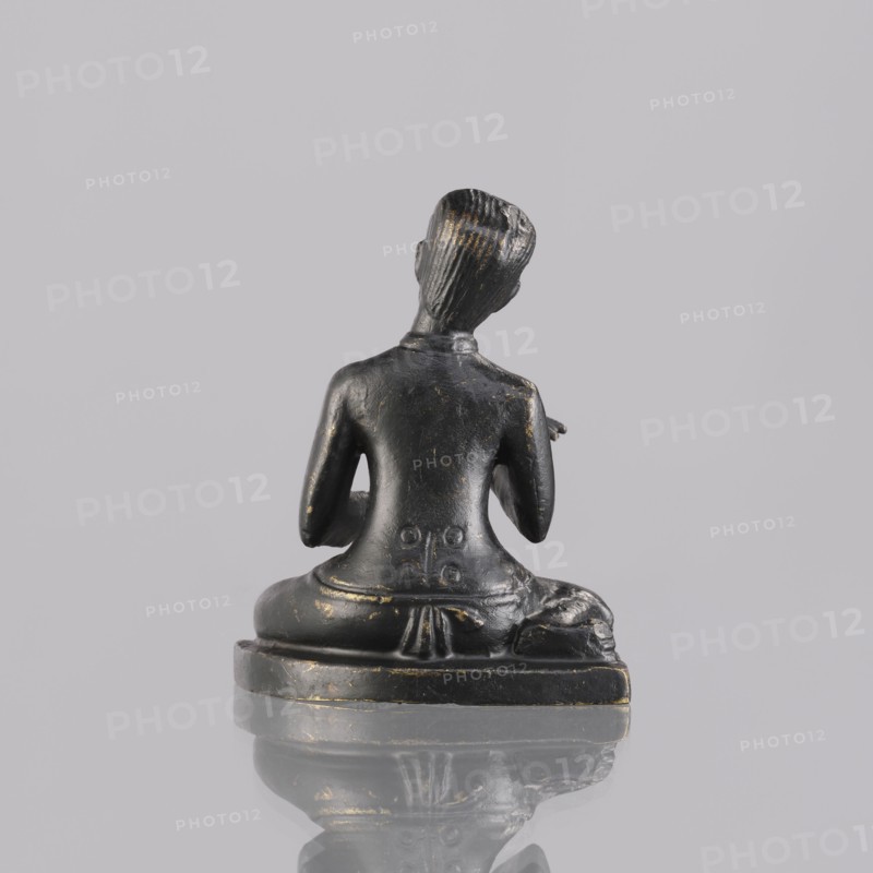 Musician figurine, Southeast Asian art, Southeast Asia culture, musicians, 1st half of the 20th century contemporary product, Cambodia place of origin, sculpture, figurine, height 6.5 cm, A small dark sculpture of a seated figure shown from the back on a flat base, with a smooth black surface and scattered spots of worn gold, the figure sitting cross-legged with arms bent at the elbows and a sculpted hairstyle with parallel grooves, the base reflecting on the glossy surface beneath, and the background a uniform light gray.