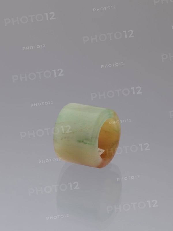 Ring, Chinese, Qing dynasty 1644–1911, green-brown jade ornament/jewelry, 18th–19th century, China; height 1.5 cm, diameter 2.0 cm., A smooth cylindrical ring with a rounded outer surface sits on a reflective surface, displaying a gradient of pale green to yellowish-orange hues with subtle marbling and a few faint darker streaks, against a plain soft gray background.