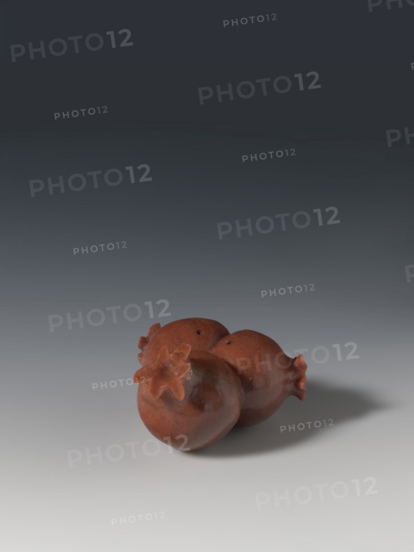 Three connected pomegranates fragment of a whole, Chinese, Qing 1644–1911, object in the shape of three connected pomegranates; each has small holes on both sides; fragment of a whole; 18th–19th century, China; sculpture; height 4.8 cm, width 8.2 cm., A group of three reddish-brown pomegranate-shaped objects sit together on a smooth surface, each with a star-shaped crown detail; the objects cast a soft gray shadow to the right and the background transitions from light gray at the bottom to dark gray at the top.