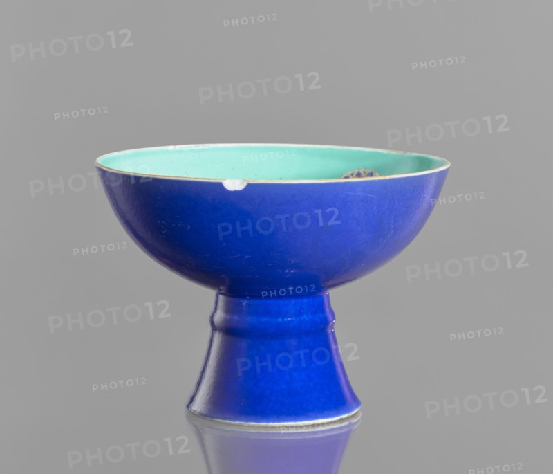 A tall footed porcelain bowl, Chinese, glazed ceramics; outer glaze stained cobalt, inner glaze green; overglaze iron hieroglyphs, overglaze enamel paints, gilding with a gilded edge. 19th century Qing Dynasty. Vessel; height 11.8 cm, diameter 16.8 cm. Maker, provenance unknown. Classification: footed bowl, decorative vessel, colored porcelain., A pedestal bowl photographed against a plain gray background, the exterior glazed in a deep blue and the interior glazed in a pale turquoise, with a thin rim showing a slightly lighter edge; the bowl sits on a tapered foot of the same deep blue and shows small areas of wear on the rim and minor surface scratches.