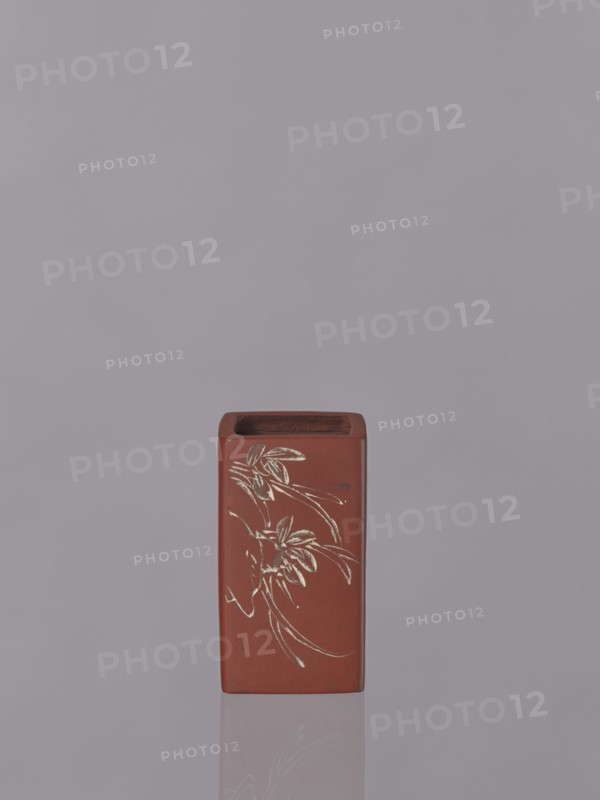 Vessel, Japanese, engraved decorations, ceramics, flowers iconography, Red-brown stoneware with engraved decoration dyed white with engobe, 19th century, Japan, vessel; height 11.1 cm, width 6.3 cm, depth 6.3 cm, A rectangular reddish-brown ceramic container with an open top sits centered against a muted gray-purple background, showing a faint reflection beneath it; the front face of the container features an etched floral design in a light contrasting color with flowing curved lines and stylized leaves, and the top interior appears darker brown.