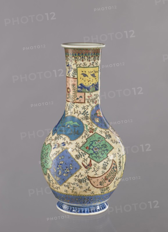 Vase, Japanese, insects, colored porcelain, butterflies, vases, floral decorations, geometric ornaments, ceramics, provenance noted, Meiji 1868–1912, cloisonné enamel, ca. 1870–1880 Meiji Period, Japan, Nagoya, vessel, height 39.5 cm, diameter 20.5 cm, A tall ceramic vase with a narrow neck and bulbous body sits against a neutral gray background; the vase displays a cream base color decorated with a patchwork of ornamental panels and medallions in blue, green, yellow, pink, and turquoise, with small black floral and vine motifs filling the spaces between panels; the neck has a band of green and red geometric pattern beneath the rim, and the lower body shows blue and green square and circular panels containing floral and landscape-like motifs, along with accents of red and brown and tiny scattered decorative elements; the foot of the vase is highlighted with a band of deep blue and lighter blue detailing.