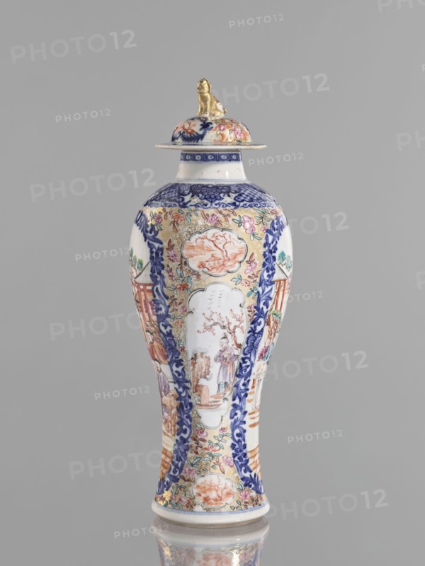 Vase with a lid, Chinese, Chinese art, ceramics; colored porcelain with figurative scenes; lid topped with a modeled seated lion. Decoration: geometric and plant ornament around the neck; two large reserves bordered with plant ornament filled with figural scenes in a landscape, two smaller reserves with figures in a landscape; background of twigs with flowers on a gold ornamental ground. White glaze, underglaze painted with cobalt; overglaze enamels in sepia, black, iron red, and gold. 18th century, China; vessel; height 28 cm; provenance unknown., The image shows a tall porcelain vase with a lid, standing against a plain gray background; the vase is predominantly white with decorative areas in blue, gold, pink, orange, green, and red, featuring ornate painted scenes and floral motifs framed by blue scrollwork, and the lid is topped by a small gold figurine.