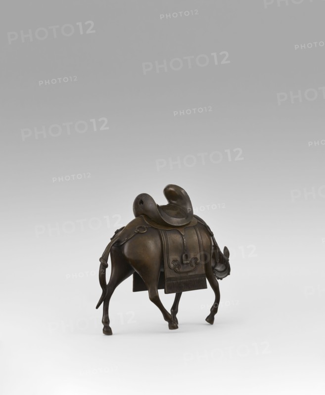 Mule with saddle - incense burner, Qing style, Chinese art, Chinese culture, mules, animals, saddle cloths, saddles, Qing 1644–1911, 19th century, China, incense burner, height 16.8 cm, A small bronze sculpture of an animal viewed from behind and slightly to one side, with a curved saddle on its back and a decorative blanket draped over its body; the animal has slender legs, a long tail that hangs down and curves, and a lowered head with visible ears and a short horn; the surface shows smooth, worn bronze tones with darker and lighter brown variations, and the background is a gradient of light gray to white.