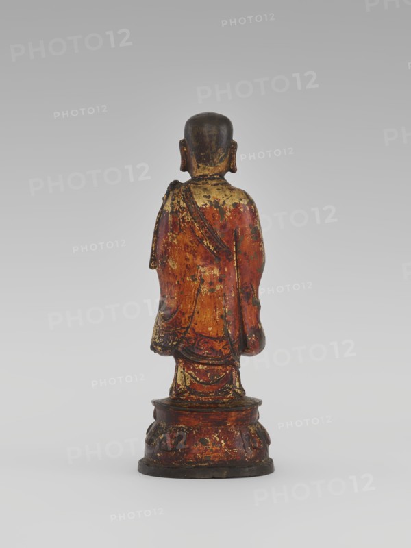 Monk, unknown role classification of creator, craftsman author; Chinese; Luohan iconography; arhat iconography; sages, monks; Buddhist art; lotus throne iconography; sculpture, figurine; Qing 1644–1911, 19th century; China; height 24.7 cm, A small standing figurine viewed from behind on a round tiered base, with a rounded head and visible ears, draped in a long robe that falls to the base; the surface shows worn areas and flaking. The visible colors include red, gold, black, brown, and a little dark green.