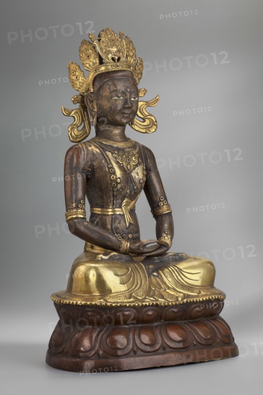 Amitayus, creator unknown, Buddhist/Tibetan/Himalayan/Mongolian art; Himalayan and Mongolian cultures; Buddha iconography with ushnisha, lotus throne, and vajras; 2nd half of the 18th–1st half of the 19th century; Inner Mongolia origin; sculpture/figurine cult object; height 37.5 cm; weight 2.12 kg., A seated statue of a figure on a rounded lotus base, rendered in dark brown and gold tones, with a dark brown body and gilded highlights on the headpiece, chest, belt, arms, and lower garment; the figure wears an ornate multi-lobed crown with decorative elements in gold and small green accents, and has stylized gold ear ornaments and flowing gold ribbons at the sides of the head; the torso shows decorative gold patterns and circular motifs, with gold bands around the upper arms and wrists and a gold sash at the waist; the hands rest in the lap in a meditative gesture and the legs are crossed beneath a draped gold lower garment that has carved folds; the lotus base is dark brown with carved...