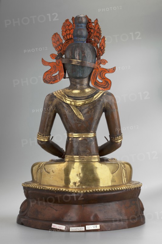 Amitayus; creator, Buddhist/Tibetan/Mongolian/Himalayan art; iconography: Buddha with ushnisha, lotus throne, vajras; 2nd half of the 18th–1st half of the 19th century; Inner Mongolia; sculpture/figurine cult object; height 37.5 cm; weight 2.12 kg, A seated statue shown from the back, with a bronze-brown body and metallic gold elements on the shoulders, waist, and seat, wearing a crown-like ornament that has bright orange-red decorative pieces and a blue-green topknot, arms resting on the lap with gold bracelets, and a rounded wooden base that is dark brown with a few lighter worn areas.