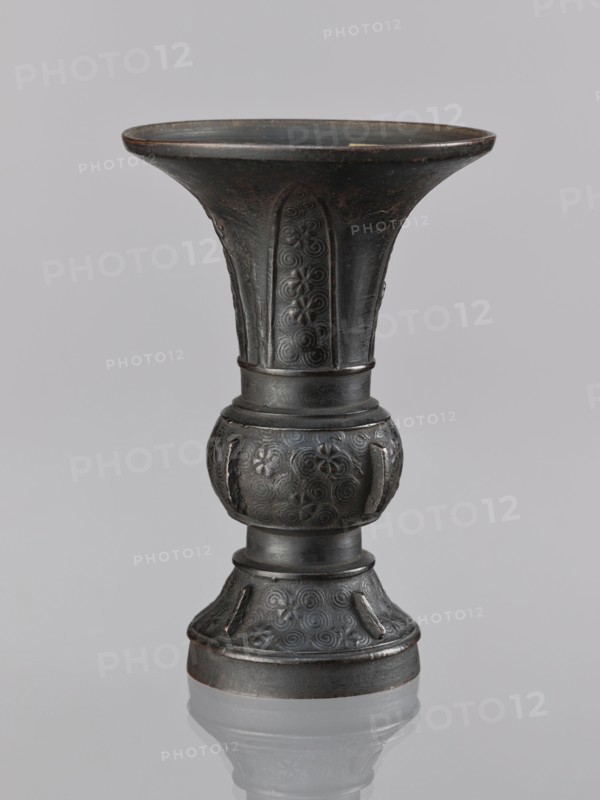 Gu-type vase gu cup, gu cups, Chinese art, Chinese culture, ceremonial/ritual vessel with spiral and plant motifs, Qing dynasty 1644–1911, 18th century, China place of origin ?, vessel; height 14.0 cm, diameter 10.0 cm, A dark metallic vase with a flared rim and a narrow waist stands against a light gray background, showing a textured surface with decorative raised patterns including spirals and floral motifs, a rounded bulbous midsection, a slightly flared foot, and subtle variations of black and dark gray with hints of brown patina.