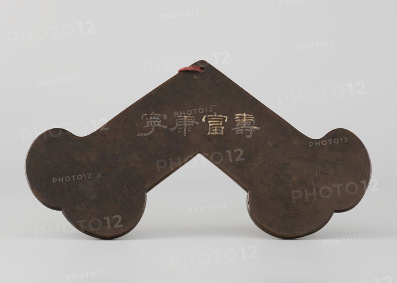 Gong, Qing dynasty 1644–1911; percussion idiophone; silver inlay; plant ornaments and tendrils; Chinese calligraphy inscription; 18th century ; China; height 15.0 cm, width 28.0 cm; musical instrument., A dark brown object with a symmetrical, angular shape and rounded ends sits against a pale gray background; the surface shows subtle lighter brown and almost black variations and faint swirling etched patterns, and a short red cord loops through a hole at the top.