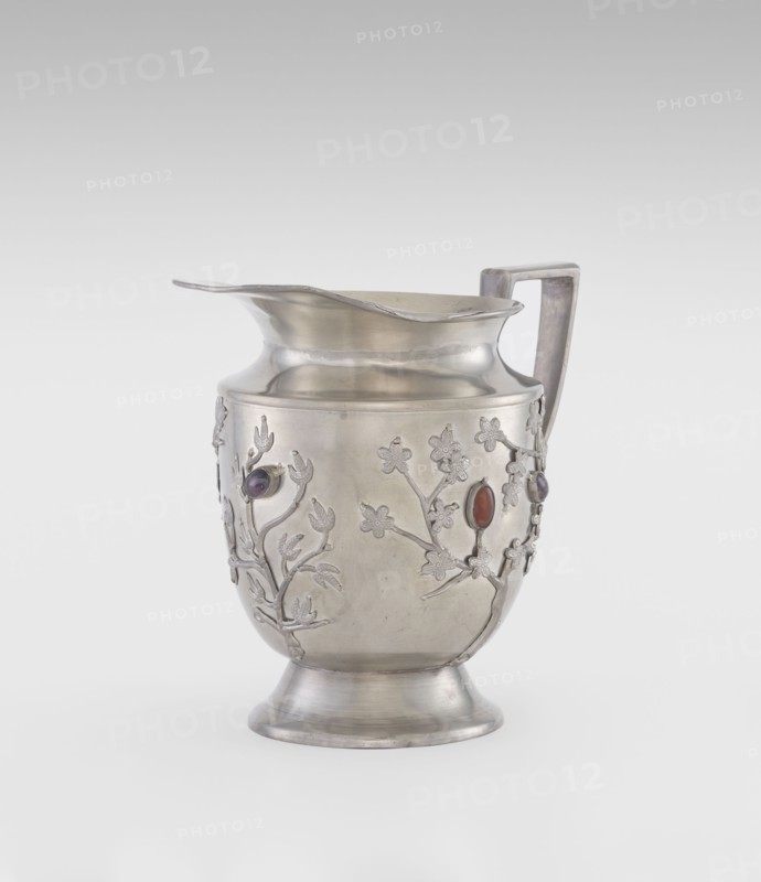Jug, plant ornament, Chinese culture, Chinese art, teapots, fruit ornament, applications, plum trees, Qing 1644–1911, applied plastic decoration: flowering leafy bunches with oval set semi-precious stones, 19th century, China, vessel; height 20.6 cm, width 23.0 cm, A metal pitcher with a curved spout and a rectangular handle stands on a flared foot; its surface is silver-colored with a slightly matte finish, and it is decorated with raised floral and branch motifs that wrap around the body, each motif incorporating a few oval stone insets in colors including purple and red.