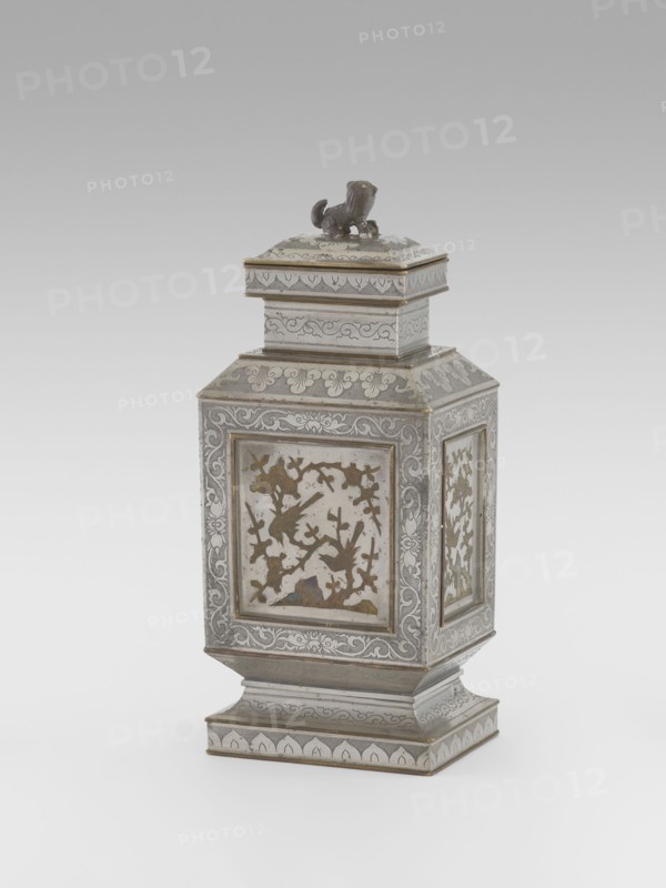 Teapot with a lid, tea, plums, birds, Chinese art, plant ornament, Chinese culture, restitution provenance, lions iconography, birds and flowers, huaniao style, fo iconography, plant twig, Qing style, clouds, Qing 1644–1911. Teapot with a profiled foot and neck, with a rectangular lid topped with a plastic figurine of a lion. Decorated with panels filled with a motif of a blossoming plum tree and birds, bordered with plant twigs the motif in the panels is engraved and set with metal. Foot, neck and cap decorated with plant ornament powdered background. 19th century, China, vessel, height 27.3 cm, width 11.5 cm, depth 8.3 cm., An ornate metal container with a square base and stepped pedestal rising to a rectangular body topped by a stacked, lidded section and a small sculpted animal finial; the surface shows intricate engraved and inlaid decorative patterns with floral and scrolling motifs, framed panels on the sides containing cutout shapes arranged as a scene of birds among branches, ...