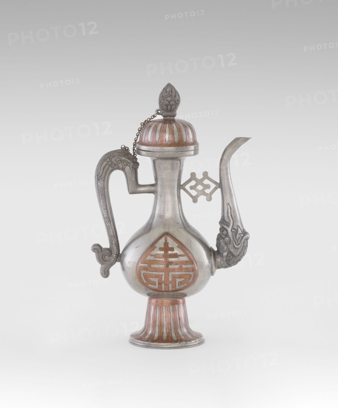 Wine jug, Chinese, plastic decorations with lotus and lotuses, longevity shou and dragons iconography, Qing 1644–1911, early 20th century, China, vessel; height 26.8 cm, width 17.5 cm, An ornate metal ewer with a rounded body on a flared, ribbed pedestal base, featuring a curved spout with a decorative animal head at its base and a sculpted handle with a curled end; the vessel has a domed lid topped by a pointed finial connected to the body by a small chain and shows inlaid or painted accents in reddish-brown against the silvery metal, with additional raised decorative motifs on the body and near the spout.