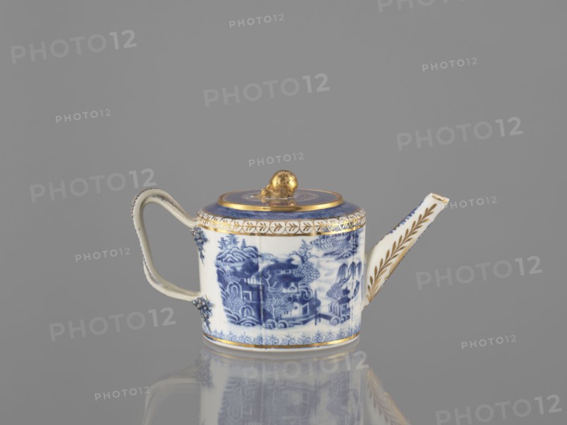 Teapot with a lid, Chinese, Qing dynasty 19th century, 1644–1912, blue-and-white porcelain teapot, ceramics; part of a 22-piece tea and coffee service teapot, 6 cups, 6 bowls, 6 saucers, a bowl, a lid, and a plate. Decoration: landscape motifs. Vessel. Height 11 cm; width 21.9 cm; diameter 11.6 cm., A small teapot is shown against a solid gray background, with a reflective surface beneath it. The teapot is white with blue painted landscape motifs and has gold accents on the lid knob, rim, and spout decoration. The handle is white with subtle blue edging and small raised floral ornaments where it attaches to the body. The spout is elongated and decorated with gold leaf-like patterns. The lid has a circular blue band and a gold knob, and the base edge has a thin gold band. The overall colors visible are gray, white, blue, and gold.