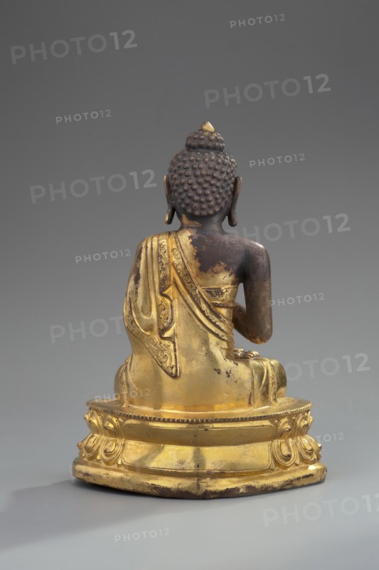 Shakyamuni Buddha, unknown sculptor, Himalayan culture, Sino-Tibetan style, Himalayan/Tibetan Buddhist art; Buddha ca. 560–480 BCE, iconography: ushnisha, lotus throne, mudras; 18th century, Tibet; sculpture, figurine; height 11 cm, width 7.7 cm, A gilded seated statue shown from behind on a rounded ornate base, with a dark brown head and shoulders featuring textured hair curls and elongated ears, and a golden robe draped over one shoulder with visible decorative patterns and worn areas; the base and lower garment are gold with some darker worn spots, and the background is a smooth neutral gray.