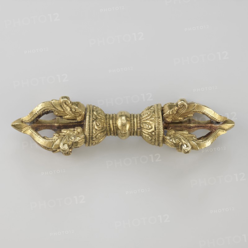Vajra;, crafted; Tibetan; Buddhist art; Tibetan Buddhist art; vajra ritual object; 19th century, Tibet; ritual object; height 9.6 cm, width 3.0 cm, A symmetrical metallic object with a gold color centered against a light gray background, featuring a rounded central section with decorative ridges and embossed patterns, flanked by two ornate tapered ends that each form a pointed, open shape with scrolling, leaf-like motifs and textured edges, showing a few areas of darker, brownish discoloration along inner surfaces.