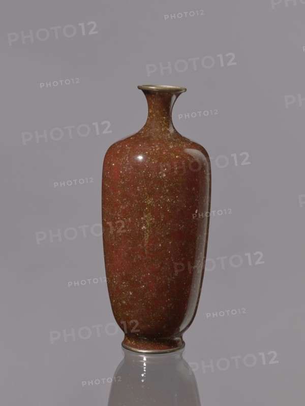 Vase, Meiji period 1868–1912, Japan. Kinseki technique. Vase with a narrow neck flaring at the spout, decorated on a brown-brick background. 19th/20th century. Vessel; height 17.9 cm, diameter 7.0 cm., A single tall vase with a narrow neck and flared rim sits centered against a plain background; the vase has a glossy, mottled surface in shades of deep red and brown with flecks of gold and darker speckles, and it casts a faint reflection on the smooth surface below; the rim and base show a thin band of a darker, metallic brownish color.