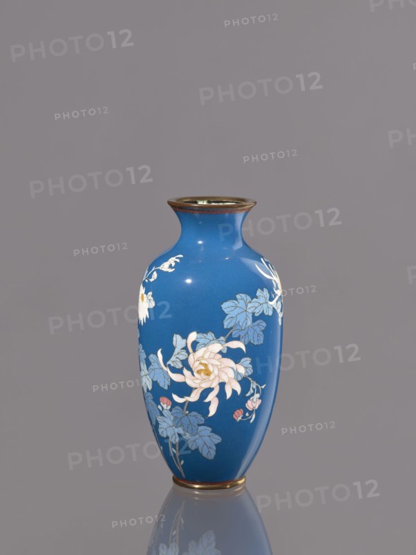 Vase with chrysanthemums, ca. 1900 Meiji 23, Japan, Nagoya; cloisonné enamel; vessel; height 18.0 cm, diameter 9.0 cm; Japanese art; Meiji 1868–1912; chrysanthemums, flowers iconography., A single blue vase with a narrow neck and flared rim stands centered against a plain gray background, decorated with floral motifs in pale pink, white, light blue, and muted green, with touches of gold at the rim and base, and a soft reflection visible beneath it.