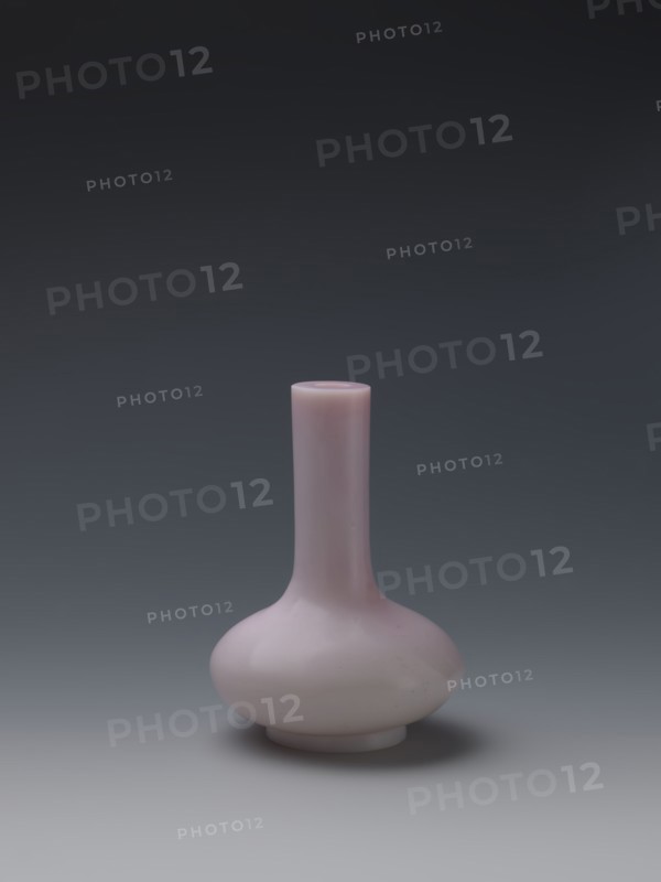 Vase, Chinese, Qing dynasty, Qianlong period 1736–1795. Flask of pale pink glass on a low ring foot with a straight long cylindrical neck. Vessel; height 13.6 cm, diameter 9.8 cm, weight 0.35 kg., A single vase with a long narrow neck and a rounded bulbous base sits centered against a smooth gradient background; the vase is a pale pink color with a glossy surface that reflects light, and the background shifts from dark gray at the top to lighter gray toward the bottom.