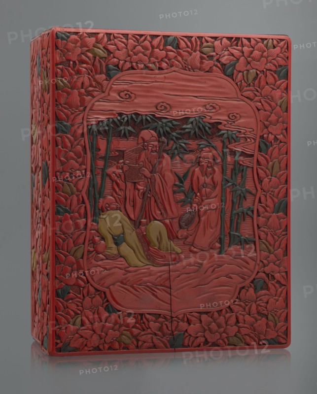 Box with a lid, Chinese art, Chinese culture, figural scenes, floral motifs, Qing 1644–1911, peonies, bamboos, geometric ornament, gourds, sages, scholars, fans, men. Decoration: on the lid a large reserve with a figural scene in a landscape; the rest of the background and sides with floral motifs. Red, black, green, and yellow lacquer, carved. 19th century, China. Container; height 13.0 cm, width 36.5 cm, depth 28.5 cm., A rectangular carved box with a predominantly red surface decorated with carved floral patterns and leafy accents in green and brown surrounds a central carved scene framed by a rounded rectangular border; the central scene depicts a group of robed figures carved in red with one reclining figure wearing a yellow robe and another seated figure wearing a yellow garment, with slender green bamboo stalks and leaves rising behind them, and stylized cloud-like carvings above; the entire object sits against a neutral gray background.