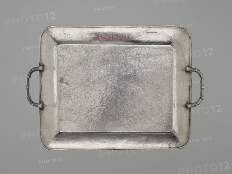 Tray, gift, Japanese art, Japanese culture, dragons, Meiji 1868–1912, Japanese dragon motif, silver, bamboos, grained background decoration, early 20th century Meiji period, Japan, vessel; height 1.7 cm, width 30.8 cm, depth 21.2 cm, A rectangular metal tray with rounded corners and a textured surface fills the image, shown against a neutral gray background; the tray has raised edges and a recessed central area with a pebbled finish, and a pair of curved handles attached at opposite shorter sides, each handle featuring segmented ridges; the metal appears mainly silver with subtle variations in tone and slight darker gray areas around the edges and handles.
