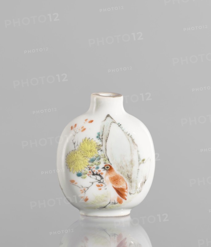 Flask — snuffbox in the shape of a pilgrim's bottle, Circular, flattened shape with a short neck. Thick porcelain body, fine-grained dough with a greyish hue, bluish glaze. Gilded rim. 19th century, China. Colored porcelain with figural scenes, images of birds, landscape motifs; moon bottle design; decorative flowers. Height 7.8 cm, width 5.1 cm., A small white ceramic vase with a rounded, flattened body and a short narrow neck sits against a plain gray background; the surface is decorated with a painted scene including a reddish-brown bird perched among branches, yellow chrysanthemum-like flowers, small orange leaves, touches of pale green and teal foliage, and a large pale beige rock-like shape, with the vase casting a soft reflection below.