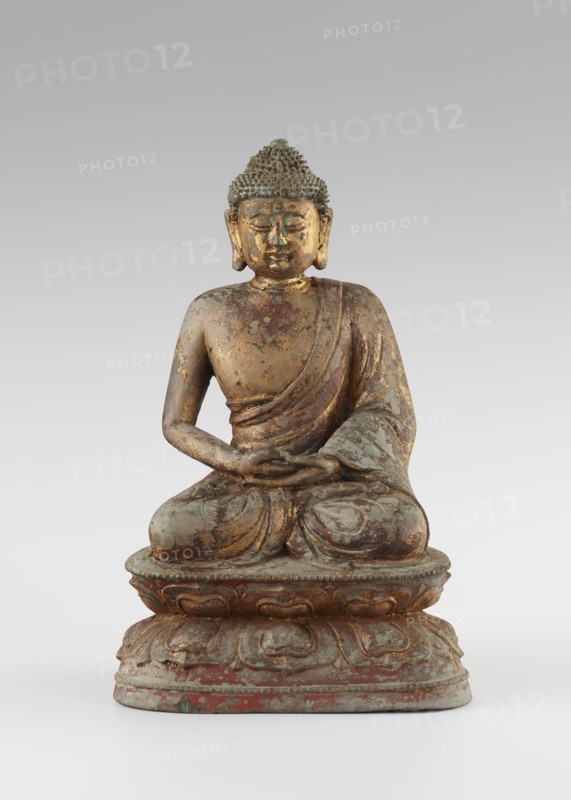 Buddha, unknown sculptor, Chinese, Qing dynasty 1644–1911, 18th century, sculpture; figurine of Buddha with ushnisha seated on a lotus throne; materials not specified; height 25.5 cm, width 16.0 cm; Buddhist art, Chinese Buddhism, lotus throne iconography, Buddha iconography., A seated statue of a figure on a tiered lotus base, shown frontally, with a textured hair surface and elongated earlobes; the figure wears a draped robe over one shoulder and has hands resting in its lap in a meditative gesture. The surface shows worn areas and peeling finishes, revealing metallic tones and patina. Visible colors include gold, greenish-blue, brown, reddish accents, and grey.