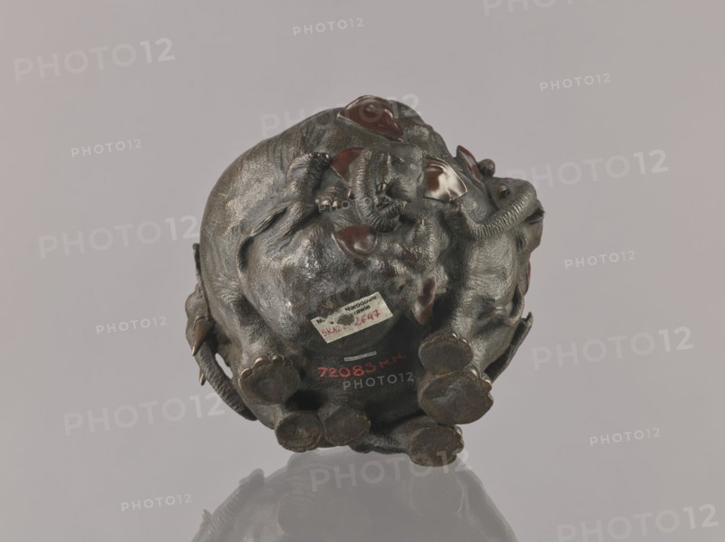 Flowerpot, ; Meiji period late 19th century, 1868–1912, Japan. Bronze flowerpot/jardiniere/vessel with copper-plated parts, decorated with elephants and other animal motifs. Height 16.0 cm, width 23.0 cm., A dark brown sculpted object resembling a cluster of animals with textured bodies sits against a pale gray background, showing glossy dark reddish-brown patches on parts of the raised surfaces and smooth rounded areas. The object casts a subtle reflection on the surface beneath it, and there are a few lighter brown highlights where the material catches the light. The overall scene includes shades of dark brown, reddish-brown, light brown, glossy reddish tones, and pale gray.