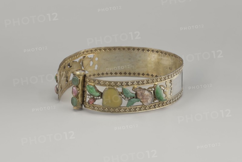 Headband, plant ornament, Chinese, Chinese art, Qing 1644–1911, head ornament, openwork inlaid with glass, semi-precious stones, river pearls and beads, 19th century, China, height 3.3 cm, diameter 12 cm., A decorative metal band with a hinged clasp lies against a pale gray background, the band showing a gold-toned finish with ornate pierced and stamped edging and an openwork central section set with decorative stones and enamel in organic shapes; visible colors include gold, green, pink, yellow, brown, and white, with glossy green leaf-shaped elements, a yellow rounded central piece, pink teardrop accents, small white bead-like details, and a brownish flower-like form, all arranged along the front panel of the band.