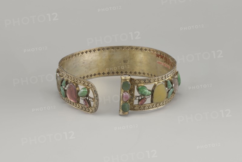 Headband, plant ornament, Chinese art, Chinese culture, Qing dynasty 1644–1911, head ornament, openwork inlaid with glass, semi-precious stones, river pearls and beads, 19th century, China, height 3.3 cm, diameter 12 cm, A gold-toned metal open bracelet with decorative cutouts and a beaded border, set with several oval and leaf-shaped stones in green, pink, yellow, and translucent pale tones, arranged in small clusters and framed by ornate filigree work, photographed against a pale gray background.