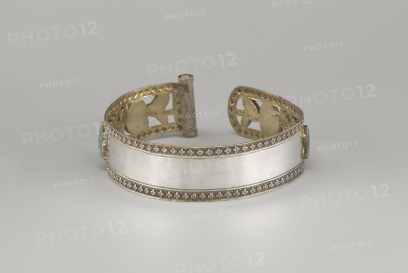 Headband, plant ornament, Chinese, Chinese art, Qing 1644–1911, head ornament, openwork inlaid with glass, semi-precious stones, river pearls and beads, 19th century, China, height 3.3 cm, diameter 12 cm, A metal cuff bracelet displayed against a gray background, featuring a central smooth silver-colored band bordered by decorative gold-colored trim with a repeating floral motif; the interior and ends of the cuff show gold-colored cutoutwork with geometric and curved shapes, and small green-colored stone settings are visible at the sides.