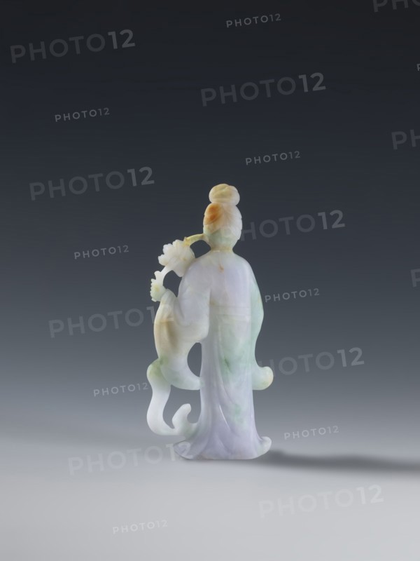 Taoist goddess?, Chinese, Qing 1644–1911, 2nd half of the 18th century. Green-pink slightly translucent jade figurine sculpture of a goddess with flowers and scepters, height 17.1 cm., A carved figurine of a standing person viewed from behind, made of a smooth, translucent stone showing pale green, lavender, white, and warm amber tones; the figure has a high bun hairstyle with amber coloring, flowing robes with soft folds and subtle green and lavender veining, and an extended arm holding a stylized flower-like object; the base of the figurine casts a soft shadow on a light grey surface against a dark grey to nearly black gradient background.