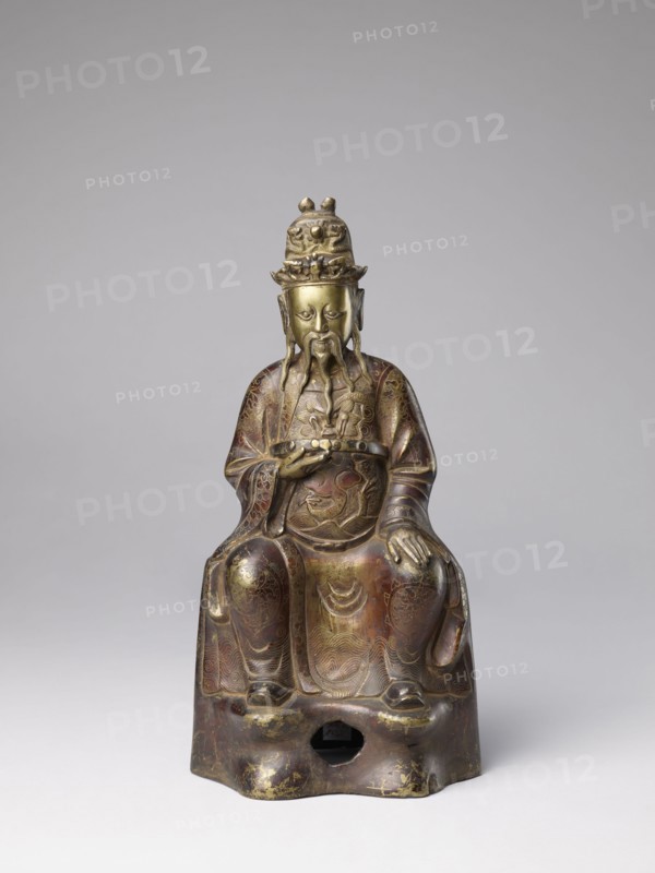 Mythical emperor, gift, Chinese art, Chinese culture, Qing 1644–1911, Qing style, figurine of a ruler wearing a dragon robe with dragon iconography, 19th century, China, sculpture; height 41.0 cm, A seated statue of a bearded figure wearing a tall ornate headdress and long flowing robes, rendered in metallic tones of gold, bronze, and brown with areas of darker patina; the figure has a long mustache and beard and holds an object in one hand while the other rests on the knee; the robes display engraved decorative patterns and wave-like motifs, and the base has a rounded opening and shows worn gold highlights and darker brown wear; the background is a smooth, neutral gray.