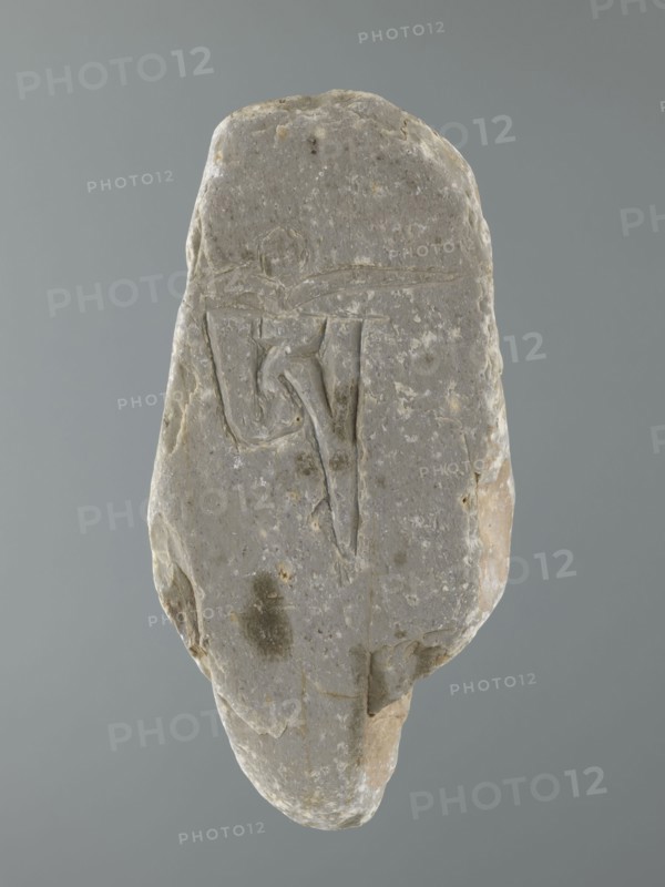 Mani stone, gift; Tibetan Buddhist ritual stone inscribed with mantras; 19th/20th century, Tibet; cult object, stone slab; height 18.3 cm, width 9.0 cm, weight 0.7 kg; Tibetan Buddhist art, Tibetan culture, Buddhism., A roughly oval stone with an irregular, weathered surface sits against a plain gray background; the stone is primarily gray with patches of lighter off-white and small areas of beige and brown, and it shows a shallow incised linear design on its face that forms angular and curved grooves; the surface has uneven texture with a few darker gray spots and subtle pitting, and the edges are chipped and rounded revealing layers of lighter beige beneath the outer gray.