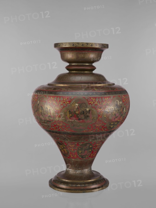 Vase, gift; Indian, 19th century. Vase with a bulging, flattened belly tapering toward the bottom; wide spout and round foot. Polychrome in red, pink, yellow, white and black. Subject motifs: gods Vishnu, Shiva, teachers, fish, plant ornaments, geometric ornaments, ascetics; functions: jug/container. Vessel; height 50.0 cm, diameter 13.0 cm, weight 5.75 kg., A rounded ornamental vessel with a flared rim and pedestal base, decorated with intricate painted scenes and floral motifs; the surface shows a metallic bronze tone with prominent red accents and touches of gold, along with darker brown and black detailing; the body features a band of rounded medallion-shaped scenes set against a red floral background, while the neck and base have carved or painted repeating leaf patterns and linear bands in bronze and brown; the overall shape tapers from a wide midsection to a narrower foot, and the finish appears glossy.