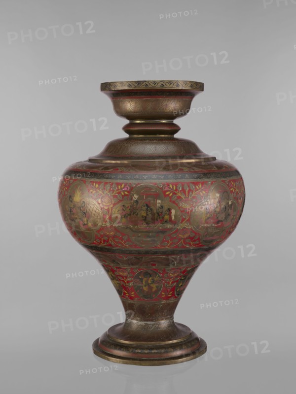 Vase, 19th century, India. Vase with a bulging, flattened belly tapering to the bottom; wide spout and round foot. Polychrome in red, pink, yellow, white and black. Decorated with jugs, gods, teachers, Vishnu, Shiva, fish, plant and geometric ornaments, and ascetics. Vessel, height 50.0 cm, diameter 13.0 cm, weight 5.75 kg., A rounded ornate vessel with a flared neck and a pedestal base, decorated with intricate painted scenes and floral motifs; the surface shows a combination of metallic brown and gold tones with prominent red areas and touches of black and green, with several circular medallions containing small figurative vignettes, bands of patterned ornament around the neck and foot, and leafy vine-like designs filling the spaces between the medallions.