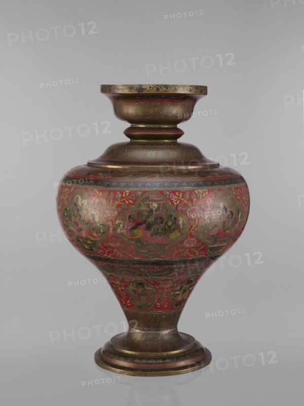 Vase, Indian, 19th century. Vessel with a bulging, flattened belly tapering toward the bottom; wide spout and round foot. Polychrome in red, pink, yellow, white and black. Decorations: gods Vishnu, Shiva, teachers, ascetics; fish; plant and geometric ornaments. Height 50.0 cm, diameter 13.0 cm, weight 5.75 kg., A rounded, ornate metal vessel with a pedestal base and flared neck is shown against a neutral background; the vessel features a dominant red field with extensive gold and brown decoration, including repeated circular medallions containing painted human figures and floral motifs, along with bands of etched patterns on the neck, shoulder, and base.