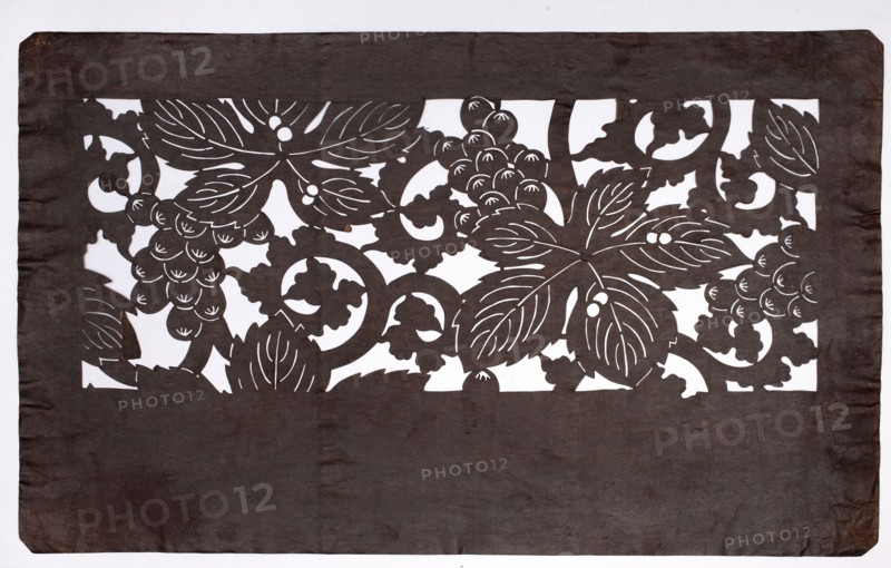 Dyeing stencil katagami with a grape and plant twig motif budô ni karakusa moyô, ise-katagami, chuban format; stencil; plant ornaments, grapes, karakusa pattern; Meiji period 19th/20th century, 1868–1912, Japan; height 40.5 cm, width 25.2 cm., A rectangular sheet with a dark brown foreground cut into an ornate horizontal band near the top, revealing a white background through an intricate pattern of large stylized leaves, curling vines, and clusters of rounded berries; the dark brown material shows uneven texture and slight wrinkles, especially toward the lower portion and edges, and the white behind emphasizes the negative-space floral design.
