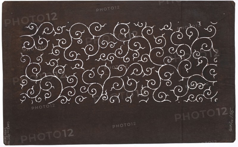 Dyeing stencil katagami with a plant twig motif karakusa, Taisho 1912–1926, ise-katagami stencil in chuban format, plant twig karakusa pattern, Japan, stencil; height 40.7 cm, width 25.2 cm, 1912–1926., The image shows a dark brown rectangular surface with a horizontal band of intricate white swirling, curling vine-like patterns across the upper half; the lower portion is mostly plain dark brown. The swirls vary in size and form a dense repeating ornamental design. The edges of the rectangle show a thin white border on two sides, and there are small lighter brown variations and tiny marks on the darker background. The visible colors are dark brown, white, and lighter brown.