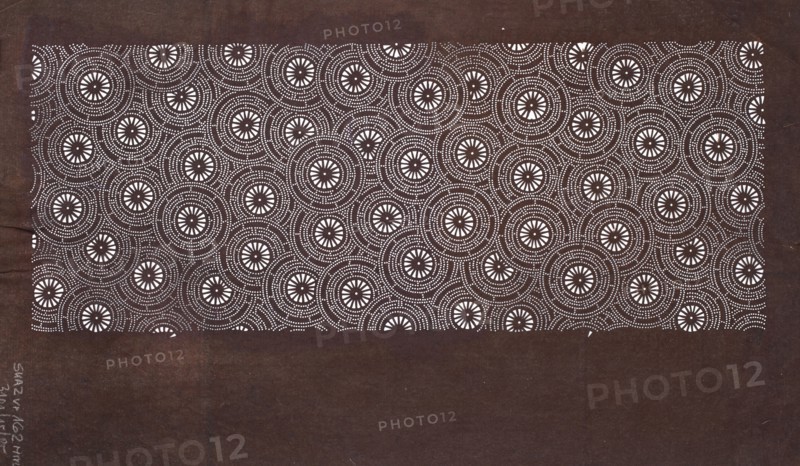 Katagami dyeing stencil with a motif of stylized floral rosettes kawari kamon moyô; ise-katagami stencil, chuban format; geometric and plant patterns; stencil; height 40.6 cm, width 24.1 cm; Japan; 2nd half of the 19th century Edo/Meiji periods., A rectangular area filled with a repeating circular dot pattern sits against a darker background; the patterned area shows concentric rings of small white dots forming circles with starburst-like white centers, and the surrounding background is a deep brown while the dots and starburst centers are white, creating a contrast between white and dark brown.