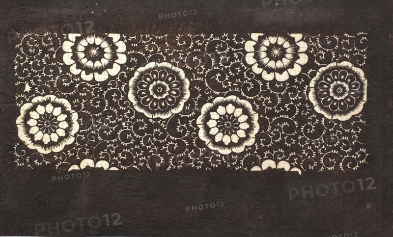 Katagami dyeing stencil with a motif of stylized flower rosettes and plant tendrils kawari kamon ni karakusa moyô, Meiji period 1868–1912, ise-katagami stencil, chuban format, karakusa pattern, floral ornaments, 19th/20th century Meiji, Japan; stencil; height 39.8 cm, width 24.0 cm., A rectangular dark brown background with a lighter central horizontal panel filled with a repeating decorative pattern; the panel contains a group of large circular floral motifs in cream and dark brown surrounded by a network of swirling vine-like tendrils in cream against the dark brown, with the lower portion of the image showing a plain dark brown area; visible colors include dark brown and cream.